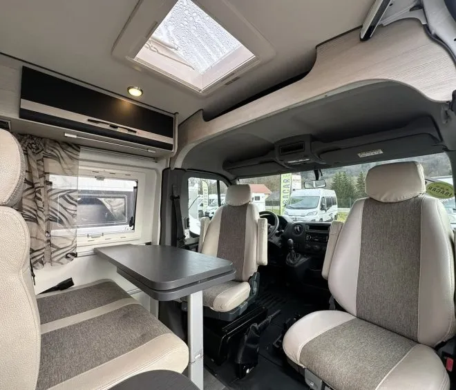 Intérieur d'un camping-car moderne avec sièges et table, vue sur l'extérieur.