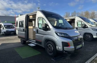 Camping-car gris avec porte latérale ouverte sur un parking