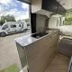 Intérieur d'un camping-car moderne avec cuisine équipée et lit, vue sur l'extérieur.