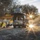 Camping-car aménagé au bord d'un lac au coucher du soleil, personne assise à côté