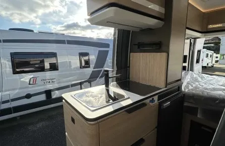 Intérieur d'un camping-car moderne avec cuisine équipée et vue sur un autre véhicule stationné.