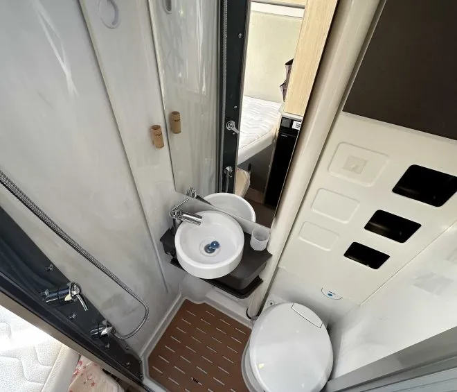 Salle de bain compacte avec douche, lavabo et toilettes dans un camping-car moderne.