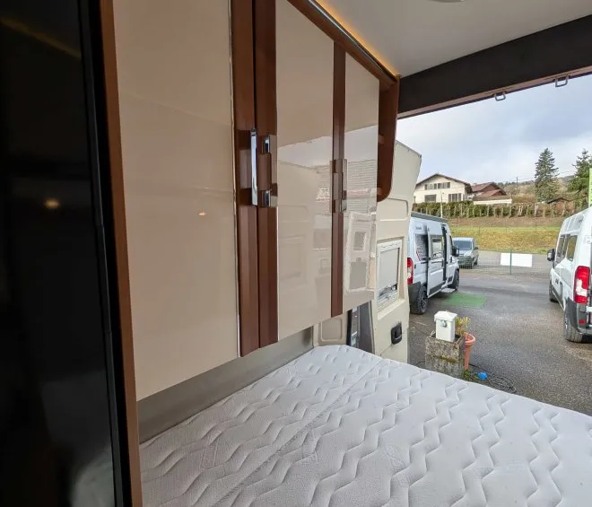 Intérieur d'un camping-car avec lit et placards en bois, stationné en extérieur.