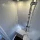 Douche moderne avec parois blanches et éclairage intégré, équipée d'une colonne de douche chromée.