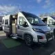 Camping-car gris avec porte latérale ouverte sur un parking