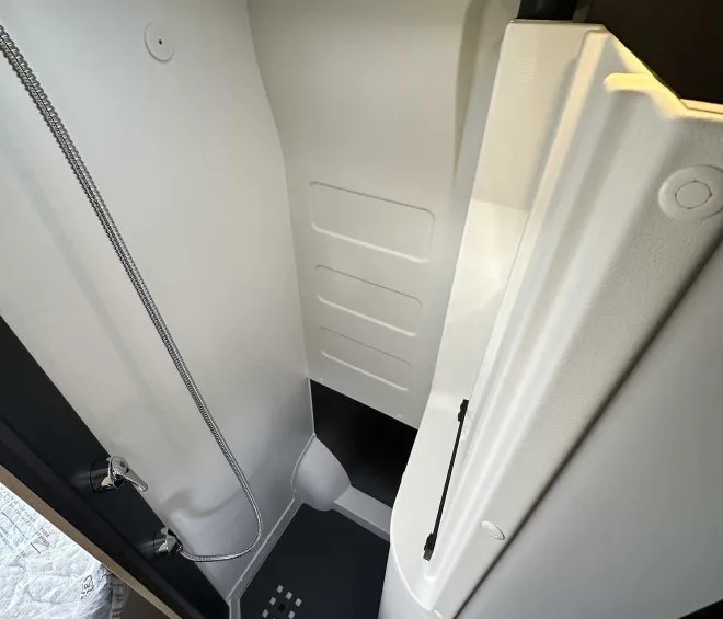 Douche compacte dans un camping-car moderne avec parois blanches et sol antidérapant.