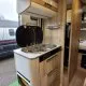 Cuisine compacte en bois dans un camping-car moderne avec plaques de cuisson et rangements.