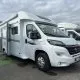 Camping-car blanc stationné sur un parking, modèle Pilote, ciel nuageux en arrière-plan.