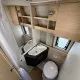 Salle de bain compacte avec lavabo, toilettes et rangements en bois clair dans un camping-car.