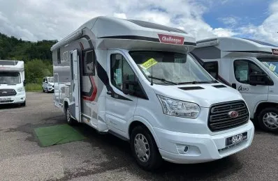 Camping-car Challenger blanc stationné sur un parking, ciel nuageux en arrière-plan.