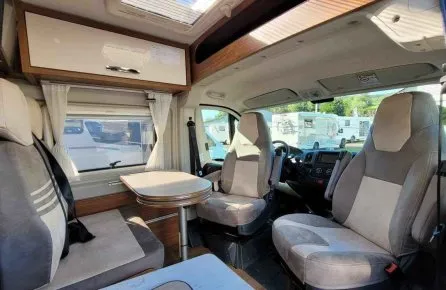Intérieur d'un camping-car avec sièges et table, vue sur l'extérieur.