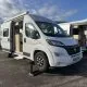 Camping-car blanc stationné avec porte ouverte, ciel nuageux