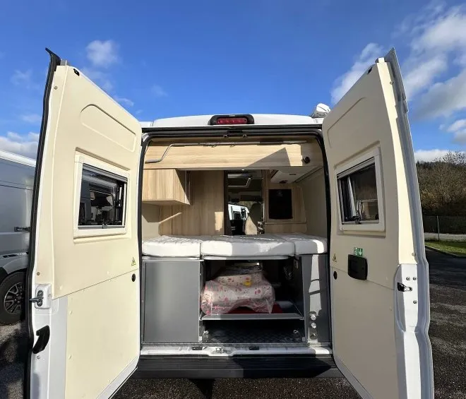 Intérieur d'un van aménagé avec portes arrière ouvertes sous un ciel bleu.