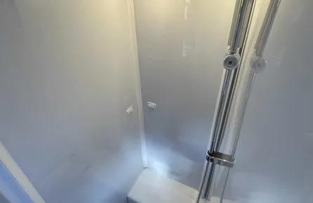Douche moderne avec parois blanches et éclairage intégré, équipée d'une colonne de douche chromée.