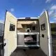 Intérieur d'un van aménagé avec portes arrière ouvertes sous un ciel bleu.