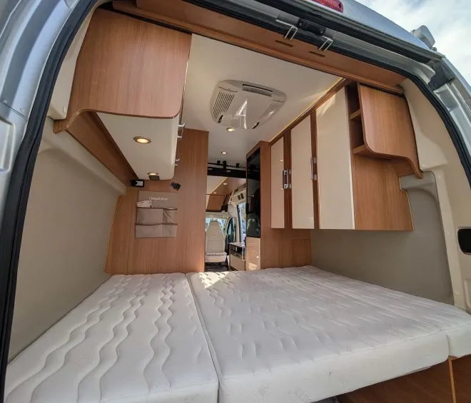 Intérieur d'un van aménagé avec lit et rangements en bois clair.