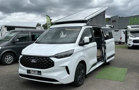 Van aménagé Ford blanc avec toit relevable sur un parking de concessionnaire.