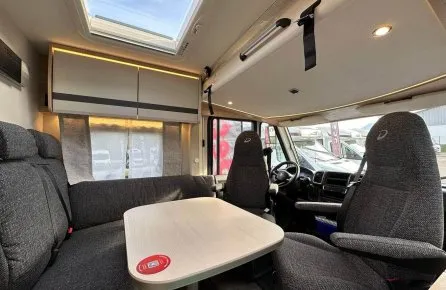 Intérieur d'un camping-car avec table, sièges et puits de lumière.