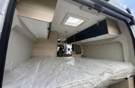 Intérieur d'un van aménagé avec lit et rangements en bois clair.
