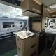Intérieur d'un camping-car moderne avec cuisine équipée et vue sur un autre véhicule stationné.
