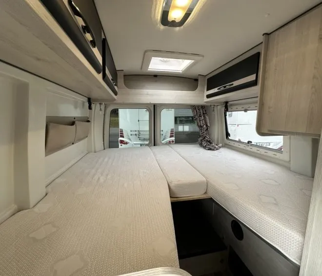Intérieur d'un camping-car avec lits jumeaux et rangements en bois clair.