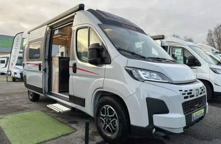 Camping-car Dethleffs blanc avec porte latérale ouverte sur un parking.