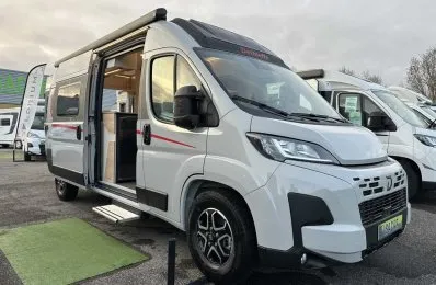 Camping-car Dethleffs blanc avec porte latérale ouverte sur un parking.