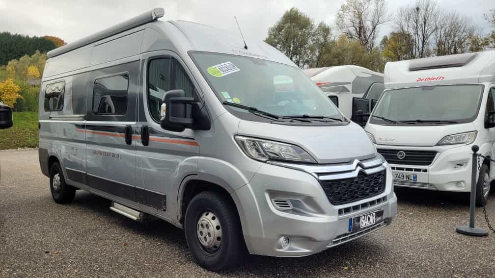 Camping-car Citroën gris stationné sur un parking avec d'autres véhicules similaires.