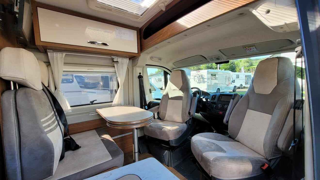 Intérieur d'un camping-car avec sièges et table, vue sur l'extérieur.