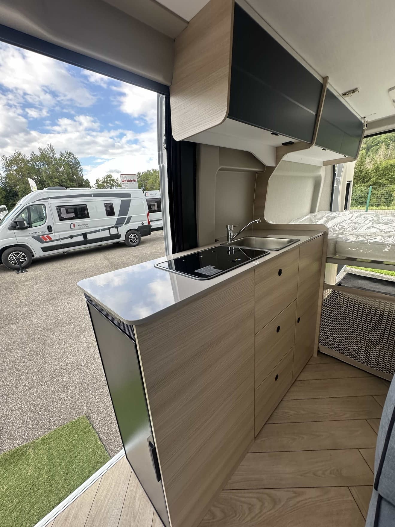 Intérieur d'un camping-car moderne avec cuisine équipée et lit, vue sur l'extérieur.