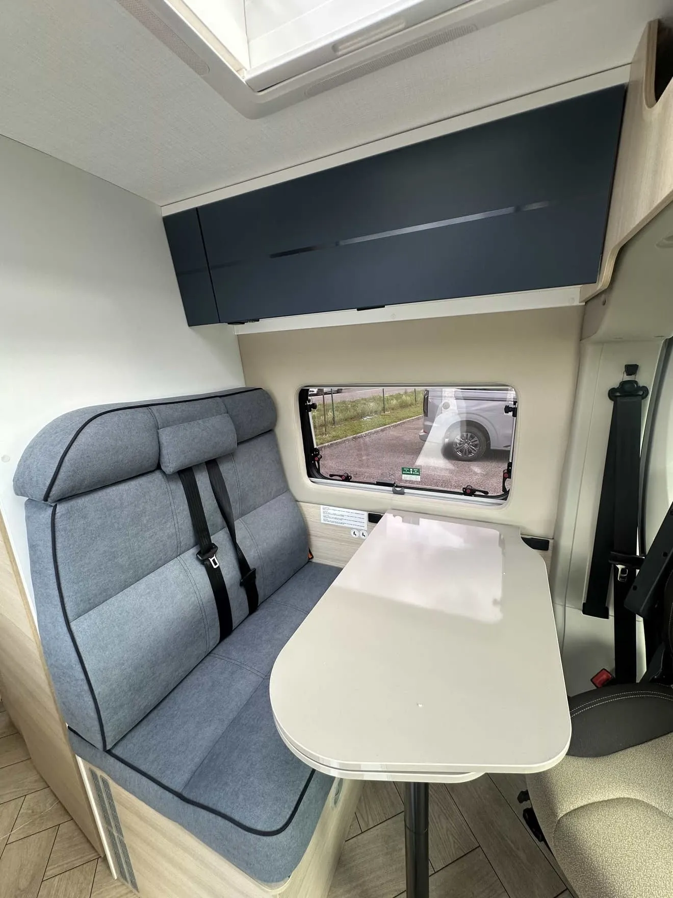 Intérieur d'un camping-car avec banquette et table pliante, vue sur fenêtre latérale.