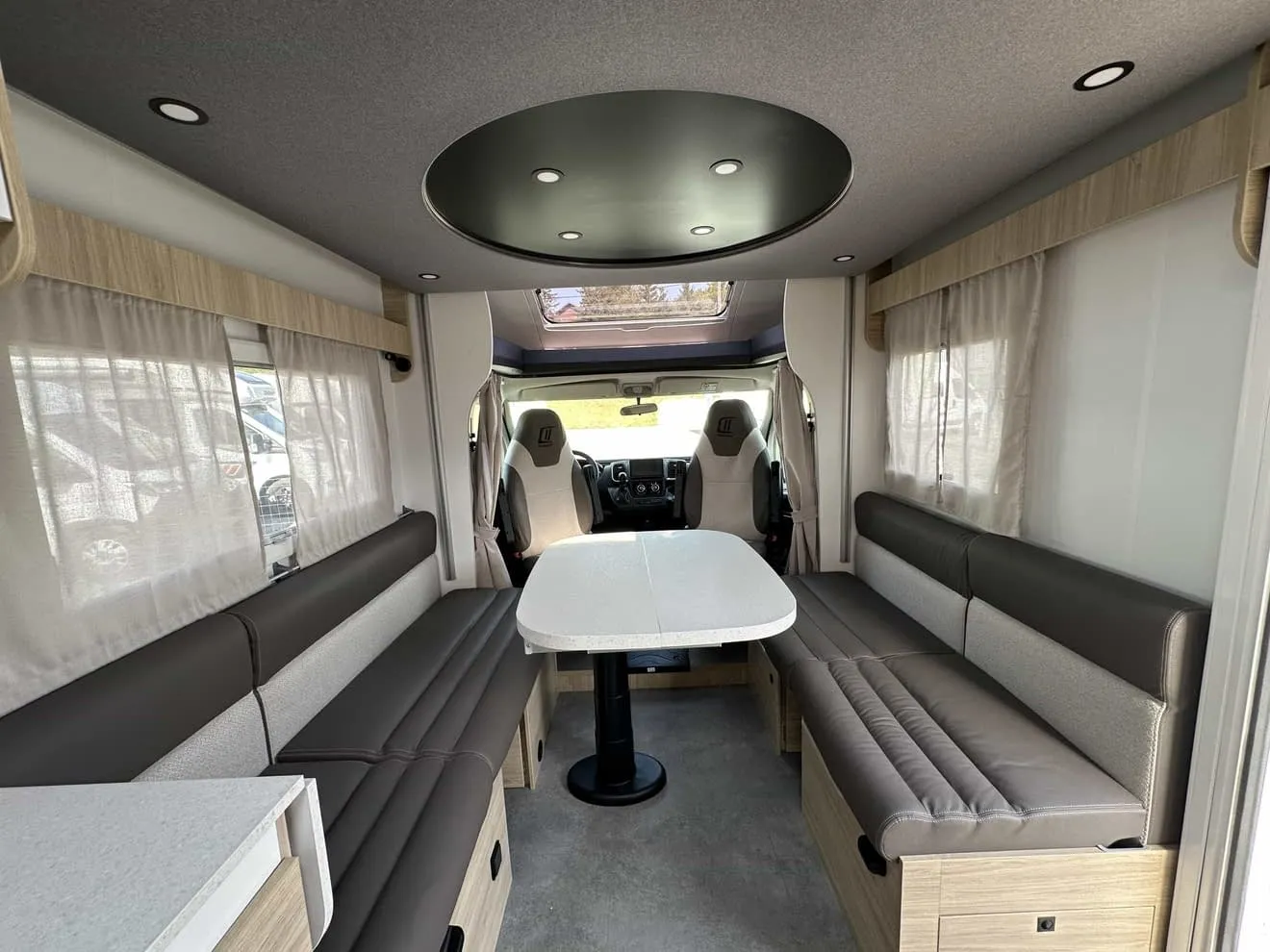 Intérieur spacieux d'un camping-car moderne avec banquettes et table centrale.