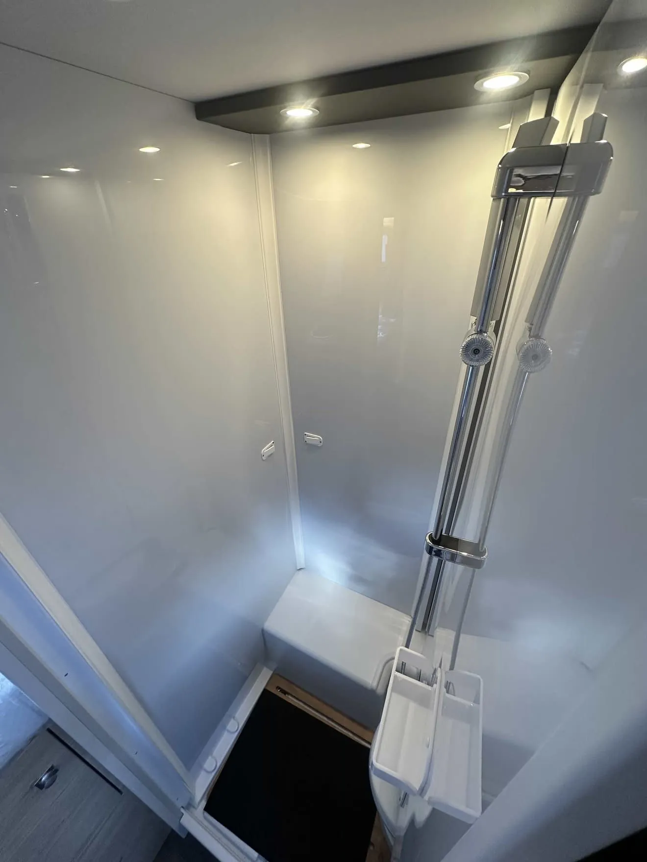 Douche moderne avec parois blanches et éclairage intégré, équipée d'une colonne de douche chromée.