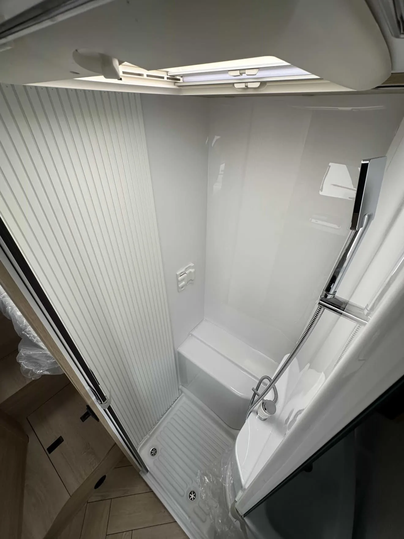 Douche compacte avec parois blanches et pommeau, dans un espace restreint de véhicule récréatif.