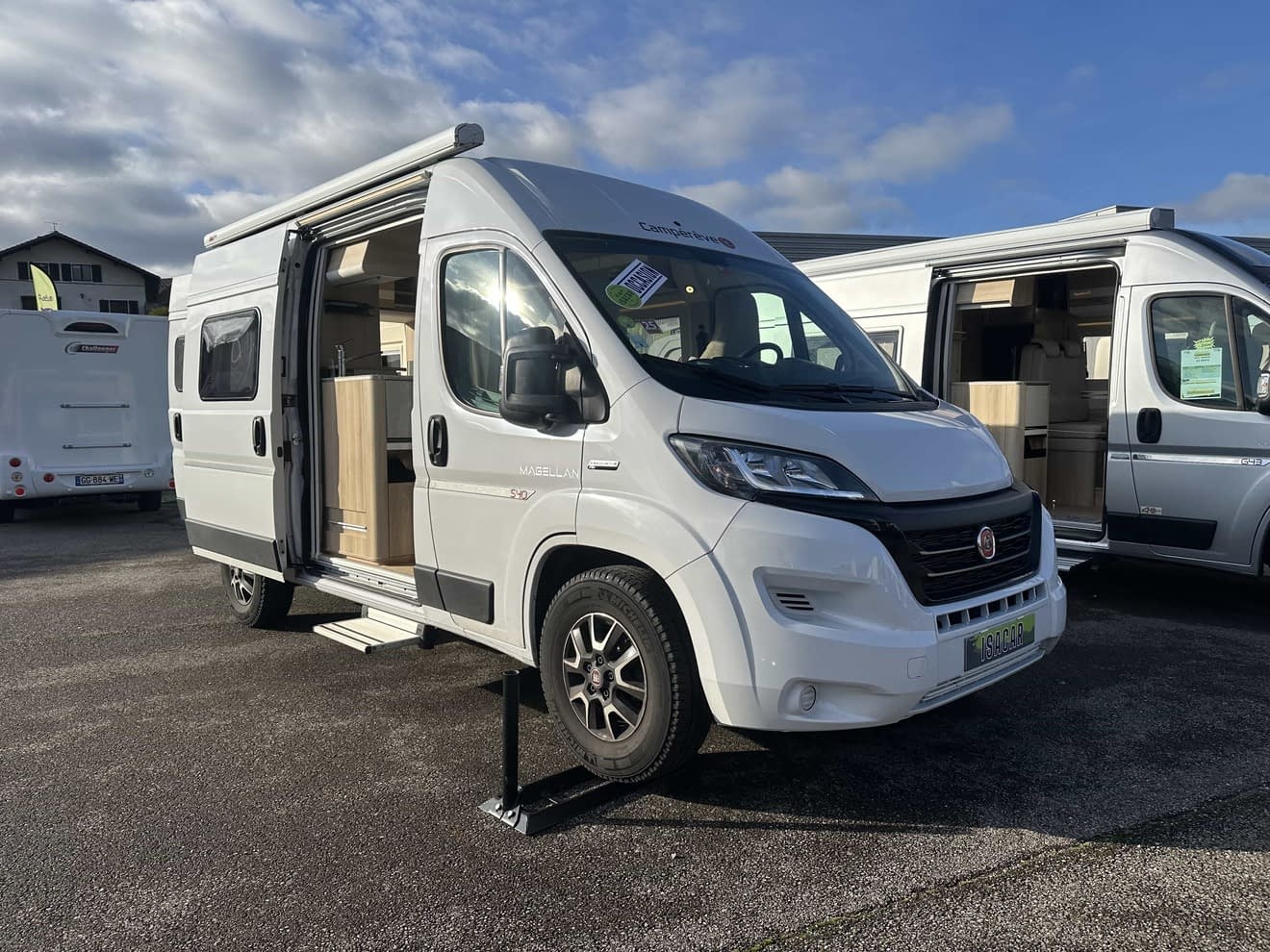 Camping-car blanc stationné avec porte ouverte, ciel nuageux
