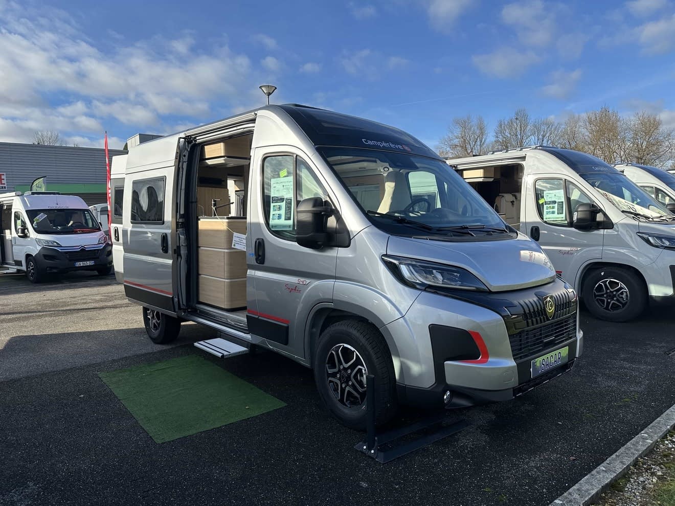 Camping-car gris avec porte latérale ouverte sur un parking