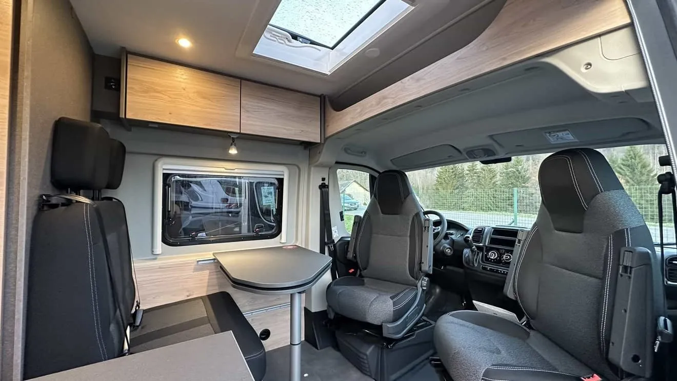 Intérieur d'un camping-car moderne avec sièges et table pliante.