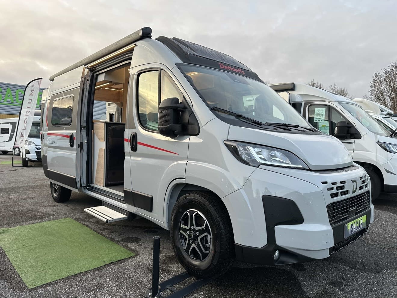 Camping-car Dethleffs blanc avec porte latérale ouverte sur un parking.