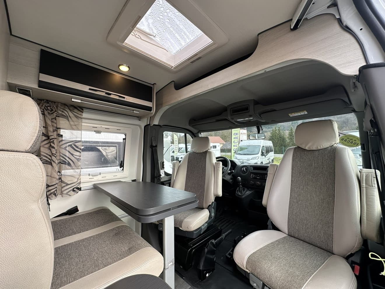 Intérieur d'un camping-car moderne avec sièges et table, vue sur l'extérieur.