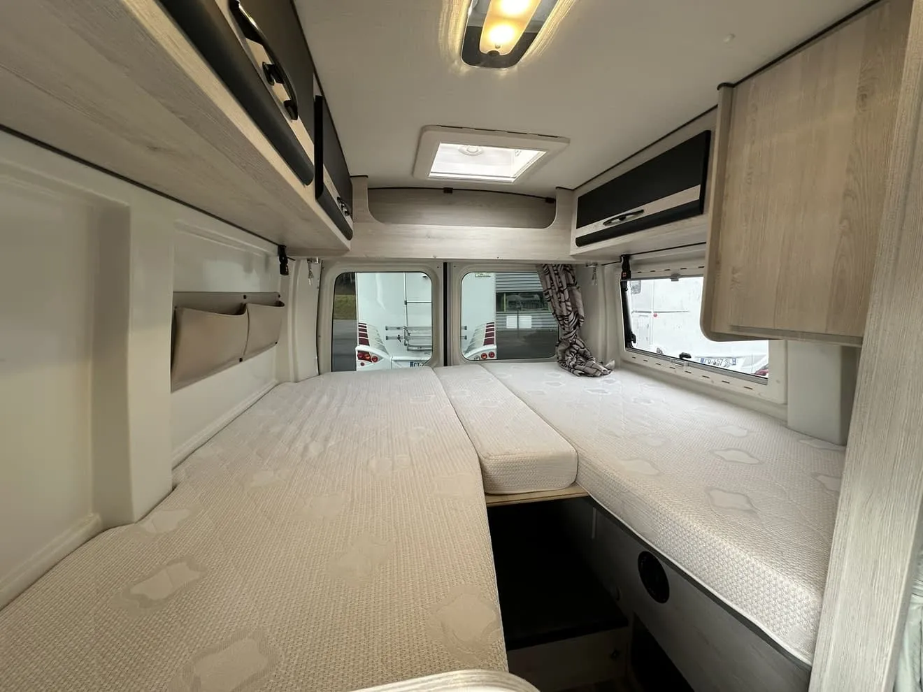 Intérieur d'un camping-car avec lits jumeaux et rangements en bois clair.