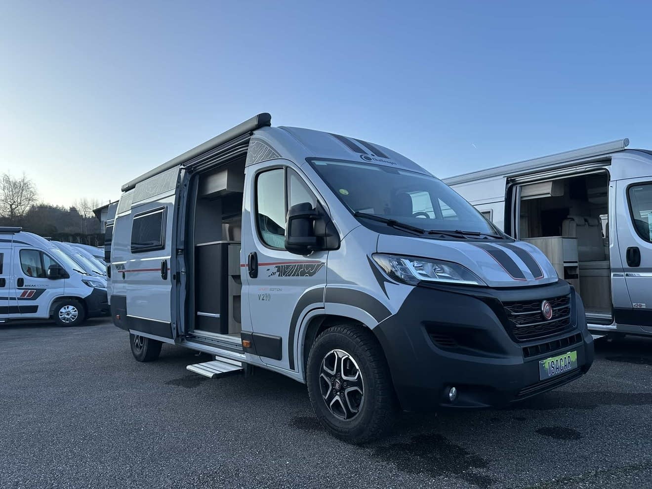Camping-car gris stationné sur un parking, porte latérale ouverte