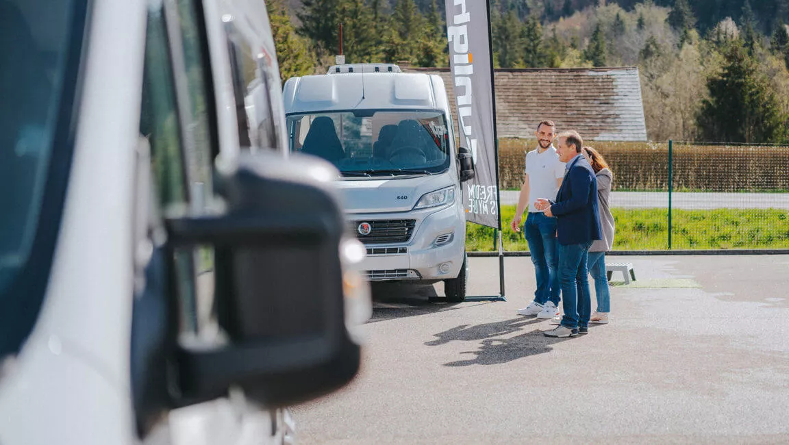 Présentation de camping-cars à des clients sur un parking en extérieur